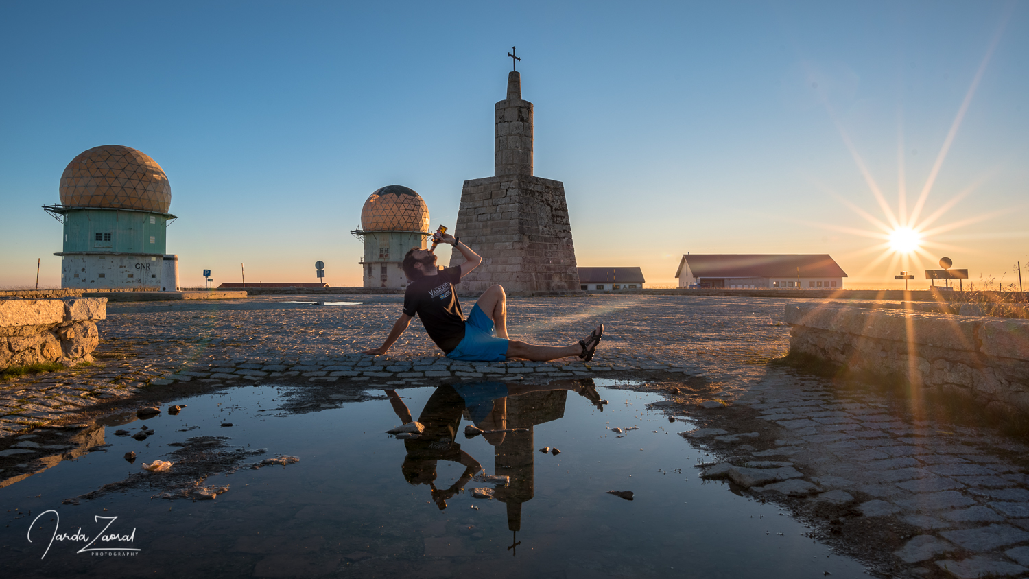 A climber drinks a beer on mountain Torre in Portugal during sunset