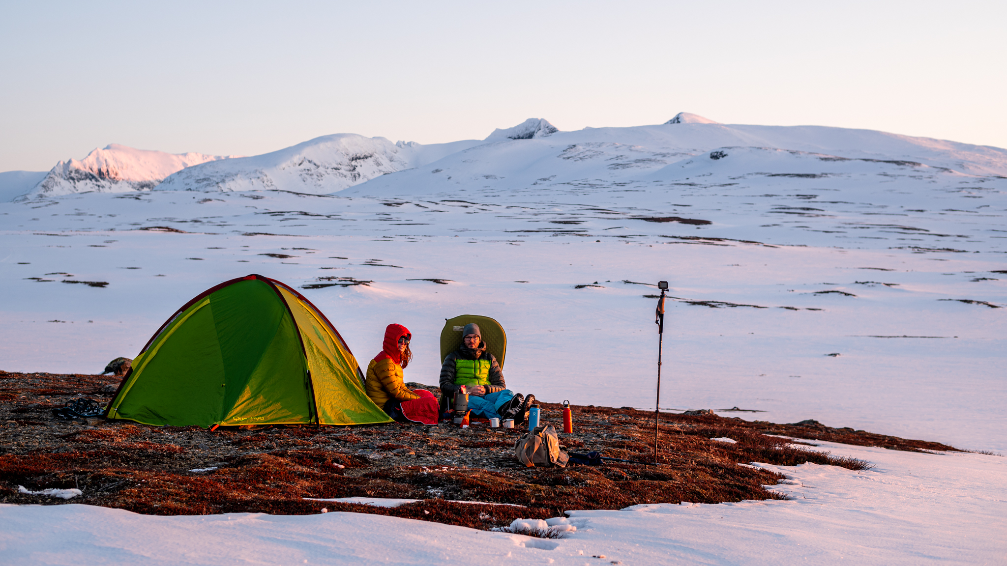 A couple enjoying sunset in a snowy valley under a mountain in Sweden